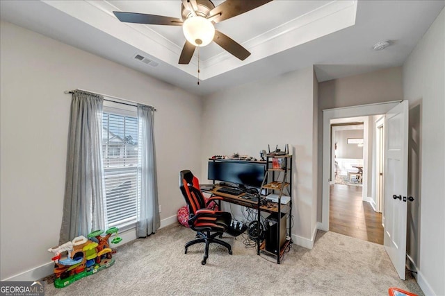 carpeted home office with ceiling fan, crown molding, and a tray ceiling