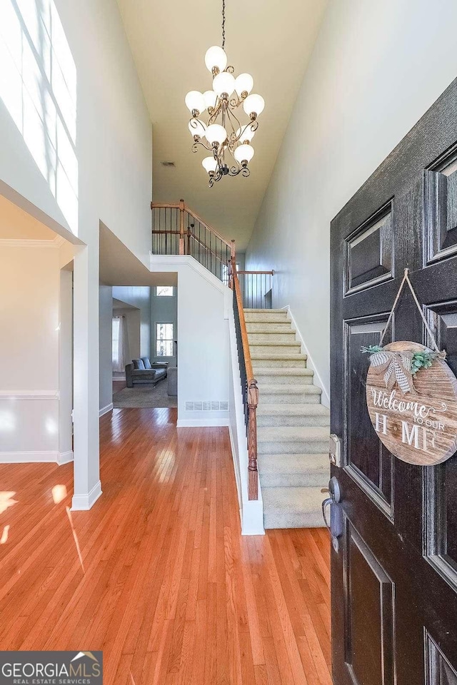 entryway with light wood-style flooring, a high ceiling, baseboards, stairs, and an inviting chandelier