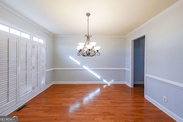 unfurnished dining area featuring a notable chandelier, wood finished floors, visible vents, baseboards, and crown molding