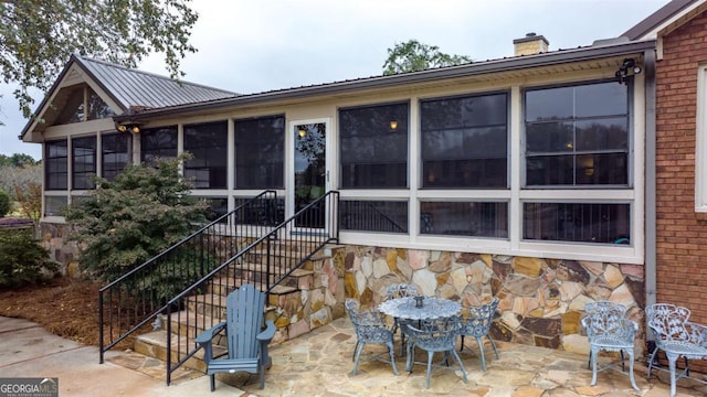 back of property featuring brick siding, a chimney, a sunroom, a patio area, and stairs