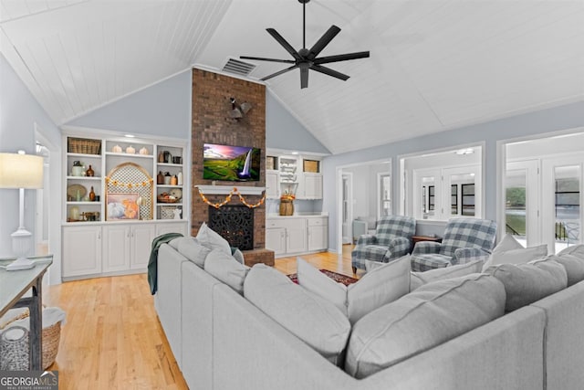 living area featuring built in features, a fireplace, light wood finished floors, visible vents, and high vaulted ceiling