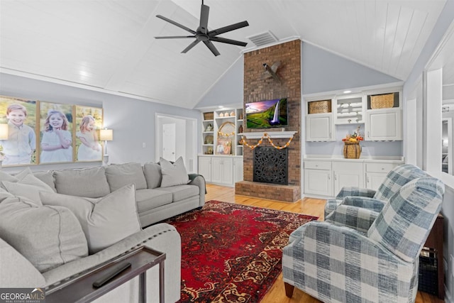 living area featuring built in shelves, lofted ceiling, visible vents, light wood-style floors, and a brick fireplace