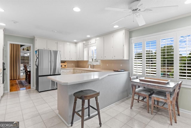 kitchen featuring white cabinets, freestanding refrigerator, a peninsula, light countertops, and crown molding