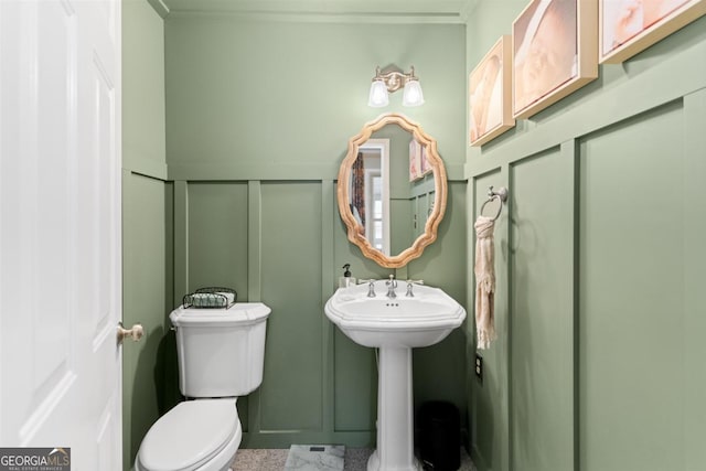 half bathroom featuring toilet, a decorative wall, and a sink