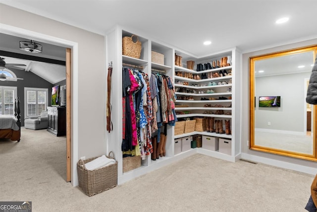 spacious closet with a ceiling fan, light colored carpet, and vaulted ceiling