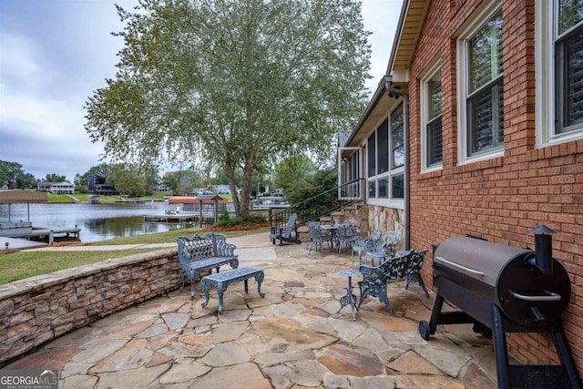 view of patio / terrace featuring outdoor dining space, a sunroom, a water view, and grilling area