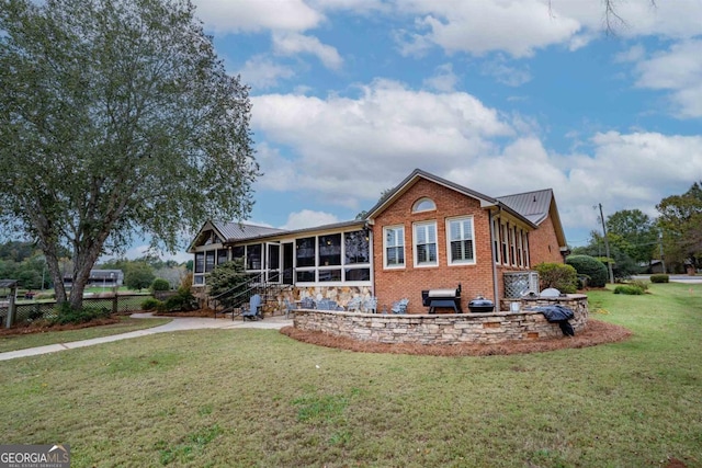 rear view of house with metal roof, brick siding, a lawn, and a sunroom