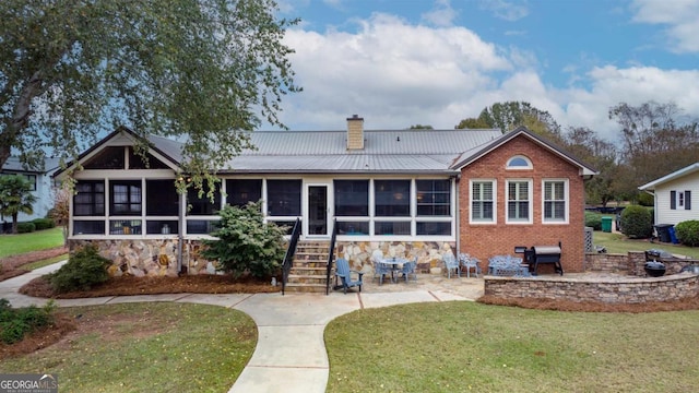 back of house with a lawn, a sunroom, a chimney, metal roof, and a patio area