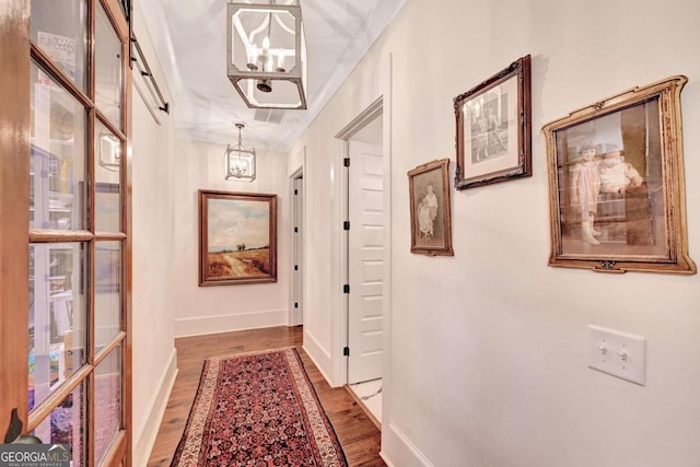 hall featuring wood-type flooring, ornamental molding, and an inviting chandelier