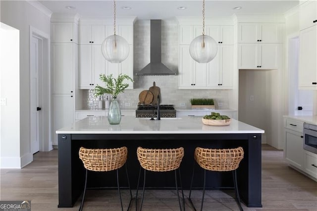 kitchen featuring white cabinetry, wall chimney exhaust hood, tasteful backsplash, stove, and a kitchen island with sink