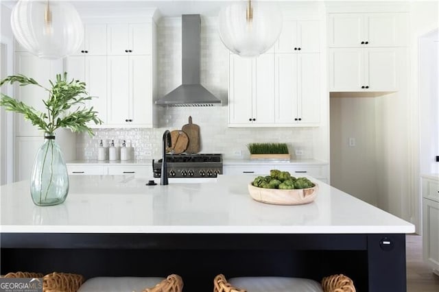 kitchen with tasteful backsplash, wall chimney range hood, pendant lighting, white cabinets, and an island with sink