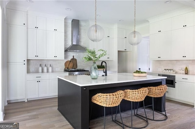 kitchen with decorative backsplash, a kitchen island with sink, pendant lighting, and wall chimney range hood