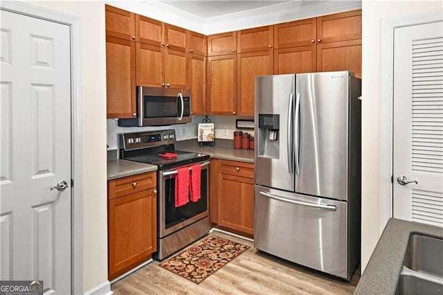 kitchen with ornamental molding, stainless steel appliances, and light wood-type flooring