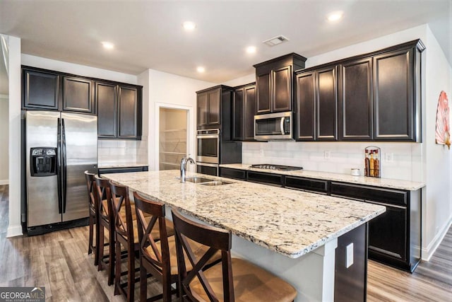 kitchen with sink, hardwood / wood-style flooring, decorative backsplash, an island with sink, and stainless steel appliances