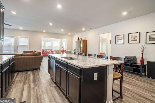 kitchen with a kitchen bar, sink, a center island with sink, dishwasher, and light hardwood / wood-style floors