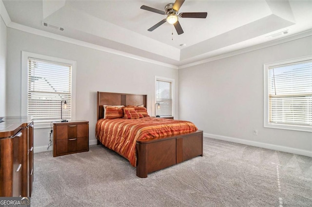 bedroom featuring ceiling fan, multiple windows, light carpet, and a tray ceiling