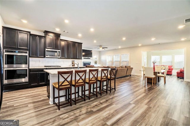 kitchen featuring a kitchen bar, an island with sink, light wood-type flooring, and appliances with stainless steel finishes