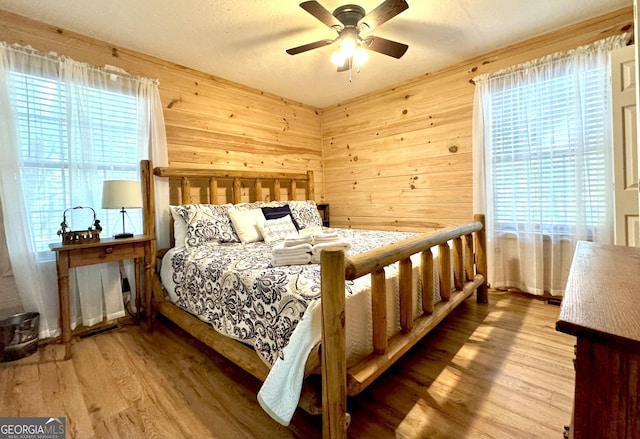 bedroom with ceiling fan, wood walls, and light hardwood / wood-style flooring