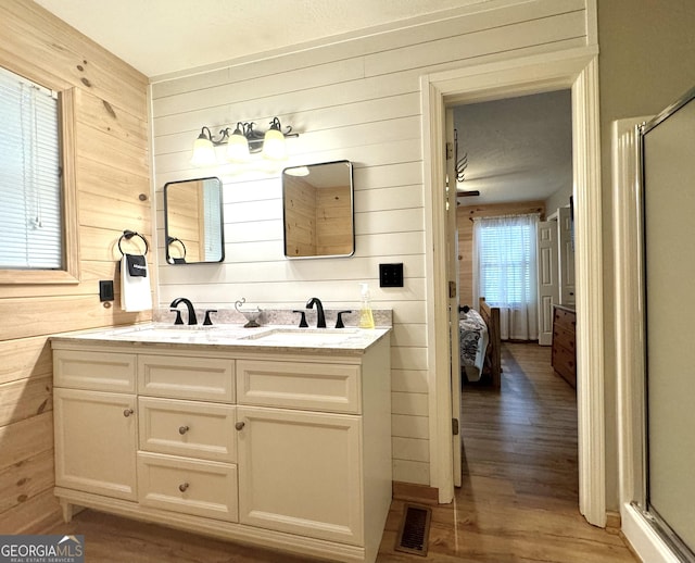 bathroom with wood-type flooring, vanity, a shower with shower door, and wood walls