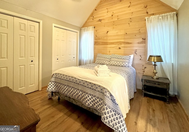 bedroom featuring hardwood / wood-style flooring, vaulted ceiling, wooden walls, and two closets