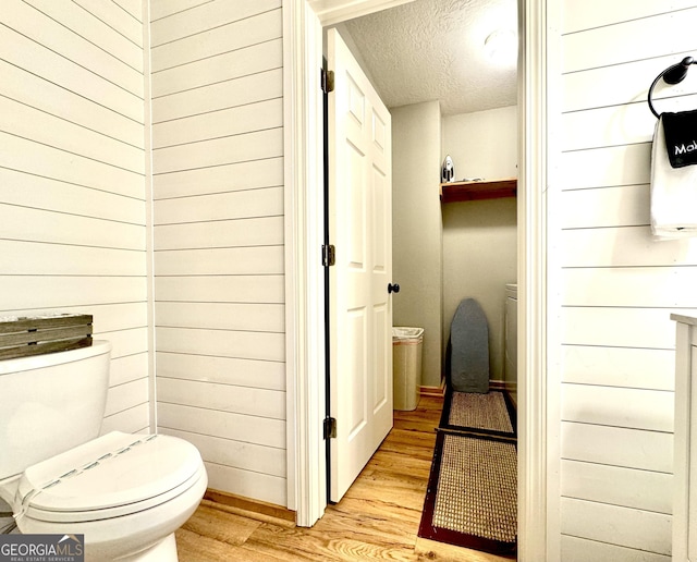 bathroom with wooden walls, hardwood / wood-style floors, a textured ceiling, and toilet