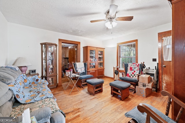 living room with ceiling fan, a textured ceiling, and light wood-type flooring