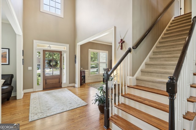 entrance foyer with a high ceiling, light wood-type flooring, and ornamental molding