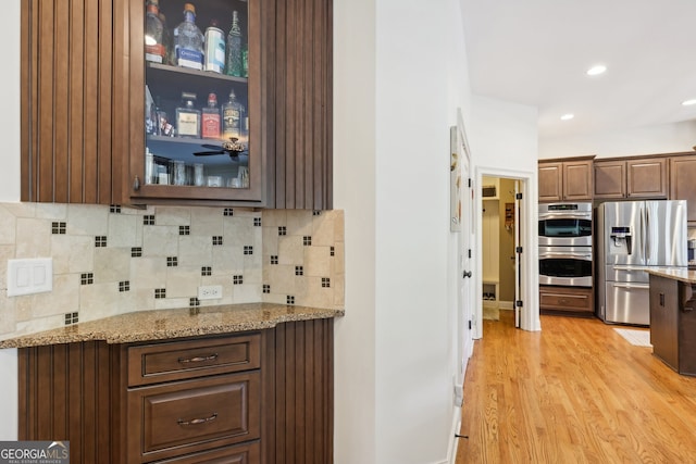 kitchen featuring light stone countertops, appliances with stainless steel finishes, tasteful backsplash, dark brown cabinets, and light hardwood / wood-style flooring