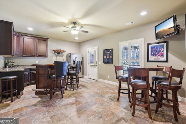 interior space featuring stainless steel fridge, dark brown cabinetry, light stone counters, and ceiling fan