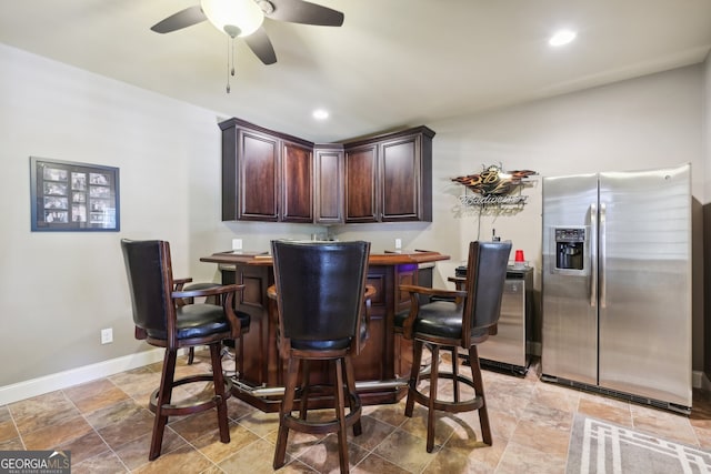 bar featuring stainless steel fridge with ice dispenser, dark brown cabinetry, and ceiling fan