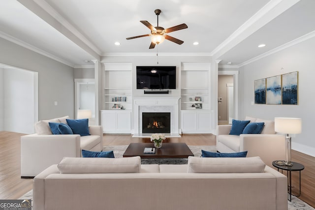 living room featuring built in shelves, ceiling fan, light hardwood / wood-style flooring, and ornamental molding