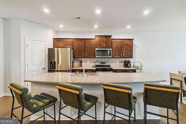 kitchen featuring a kitchen breakfast bar, dark hardwood / wood-style floors, stainless steel appliances, and a kitchen island with sink