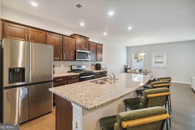 kitchen with appliances with stainless steel finishes, a breakfast bar, sink, a center island with sink, and decorative light fixtures