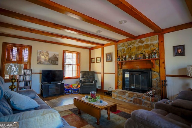 living room featuring beam ceiling, light wood-type flooring, and a stone fireplace