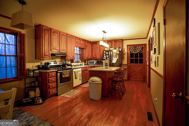 kitchen featuring a center island, decorative light fixtures, dark wood-type flooring, appliances with stainless steel finishes, and a breakfast bar area