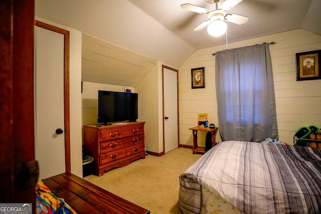 bedroom with vaulted ceiling, wooden walls, light colored carpet, and ceiling fan