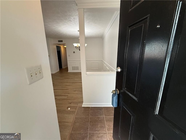 corridor with dark tile patterned flooring, ornamental molding, a textured ceiling, and an inviting chandelier