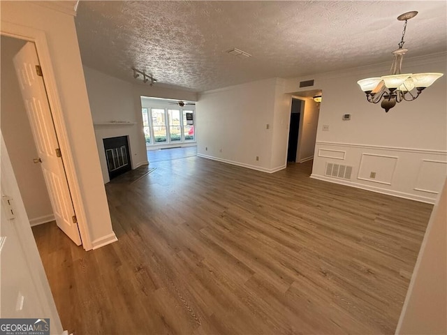 unfurnished living room with a chandelier, a textured ceiling, track lighting, and dark wood-type flooring