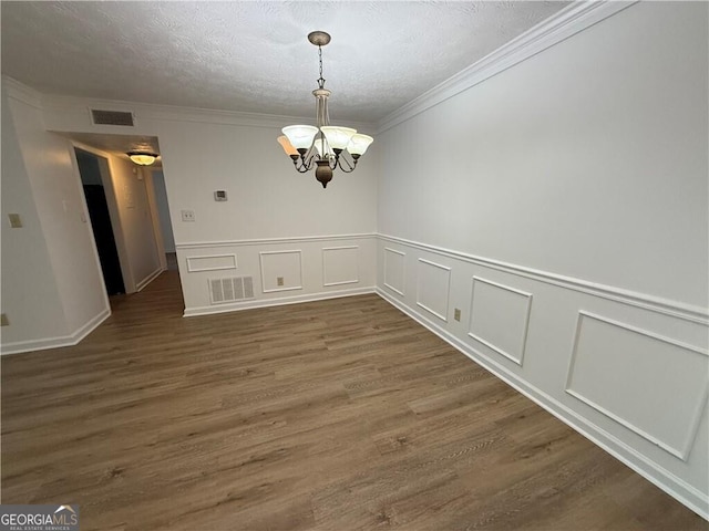 unfurnished dining area with a textured ceiling, dark hardwood / wood-style flooring, crown molding, and an inviting chandelier