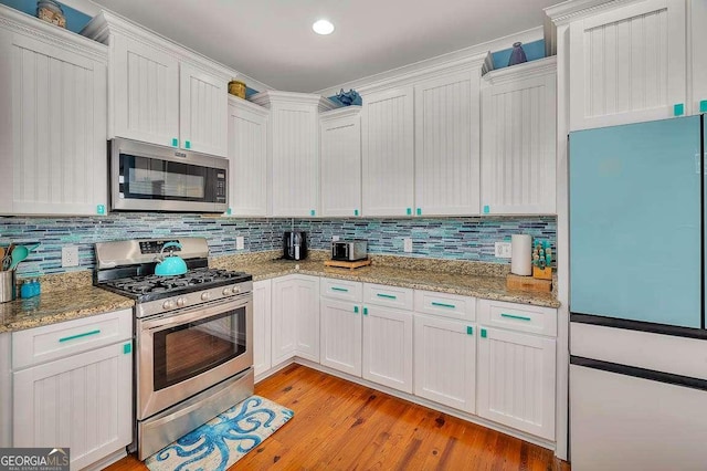 kitchen with white cabinets, stainless steel appliances, light stone countertops, and light hardwood / wood-style floors