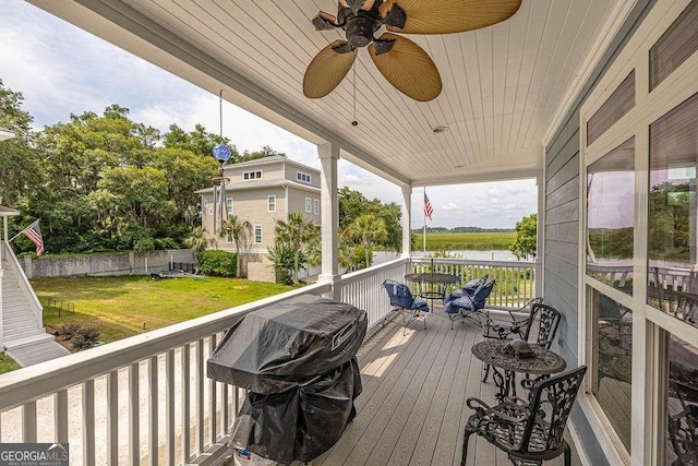 deck featuring a lawn, area for grilling, ceiling fan, and a water view