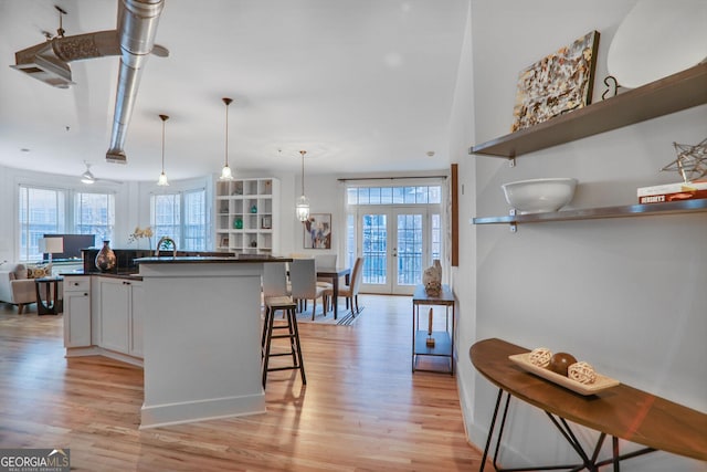 kitchen featuring french doors, light hardwood / wood-style floors, a kitchen breakfast bar, and decorative light fixtures