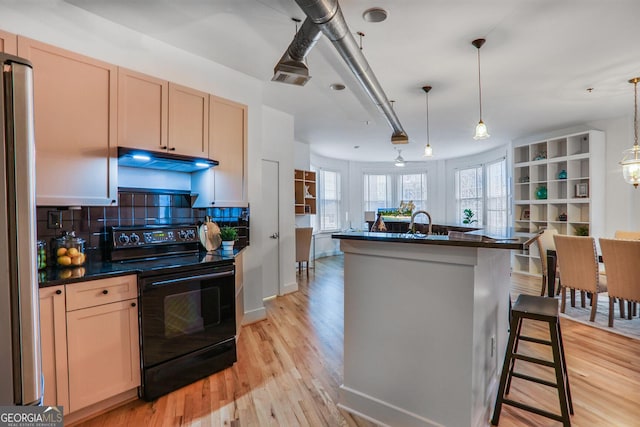 kitchen featuring light brown cabinetry, a kitchen bar, hanging light fixtures, a center island with sink, and black / electric stove