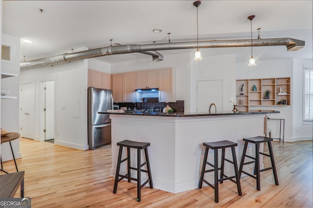 kitchen featuring light brown cabinetry, hanging light fixtures, stainless steel refrigerator, and light wood-type flooring