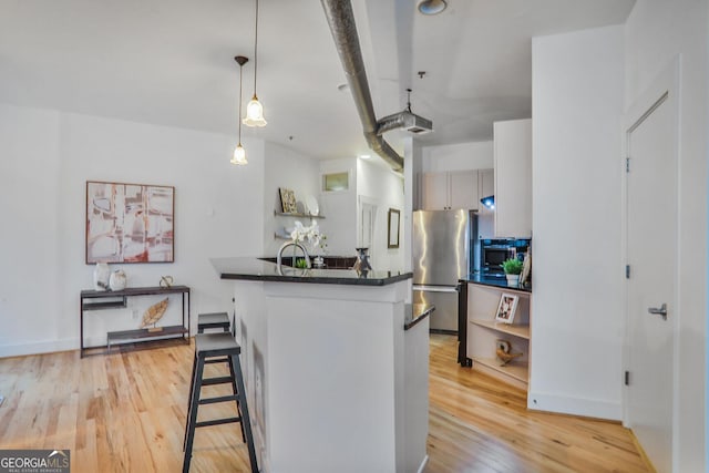 kitchen with stainless steel refrigerator, hanging light fixtures, light hardwood / wood-style floors, a kitchen bar, and kitchen peninsula