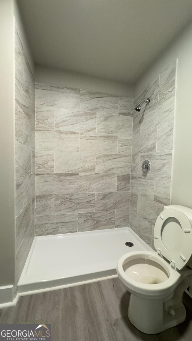 bathroom featuring a tile shower, toilet, and wood-type flooring