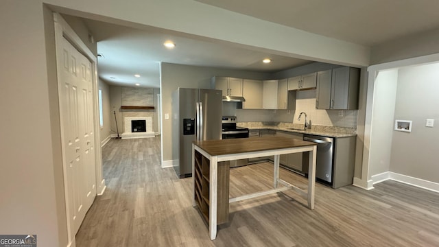 kitchen with gray cabinetry, sink, light hardwood / wood-style floors, a large fireplace, and stainless steel appliances