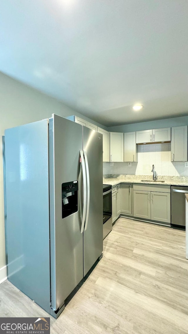 kitchen with gray cabinetry, sink, decorative backsplash, light hardwood / wood-style floors, and stainless steel appliances