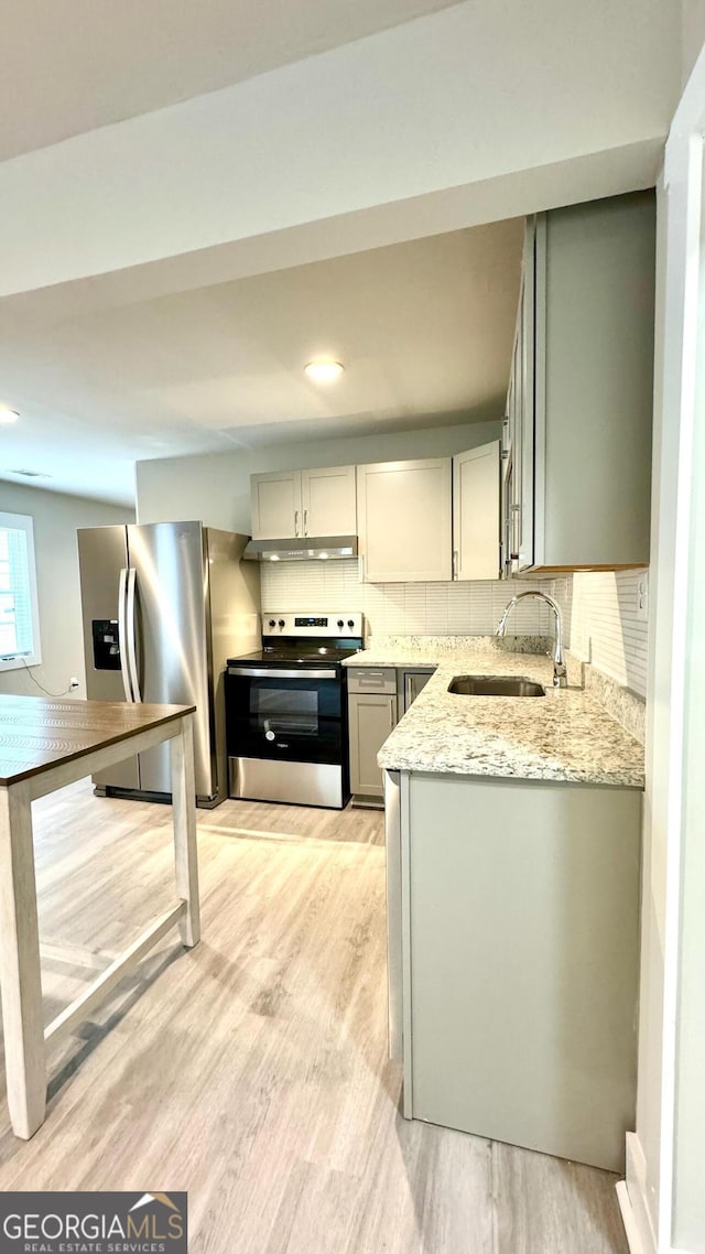 kitchen with backsplash, sink, light wood-type flooring, light stone countertops, and appliances with stainless steel finishes