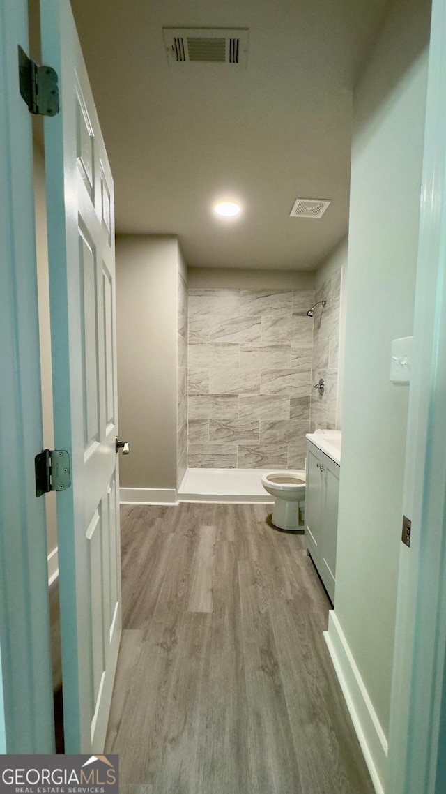 bathroom featuring hardwood / wood-style floors, vanity, toilet, and tiled shower